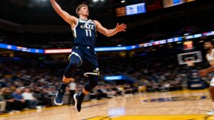Lauri Markkanen shooting a basketball during an NBA game wearing Utah Jazz jersey in a packed arena.